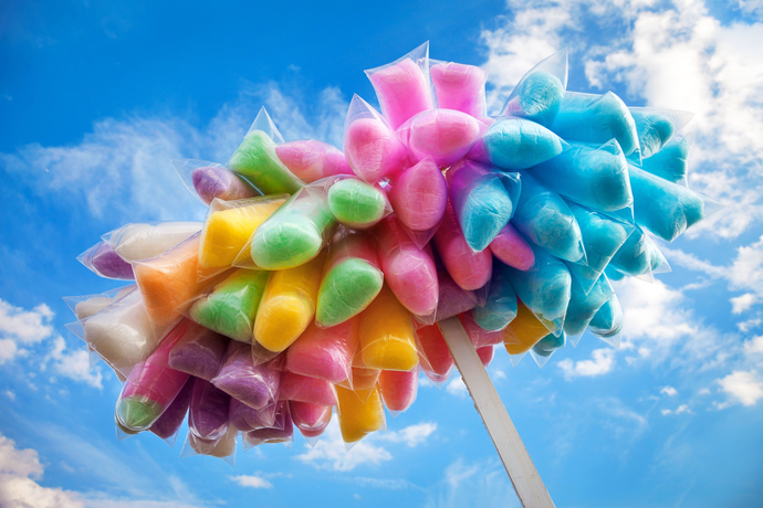 vendor pole filled with multi colored cotton candy against blue sky with puffy clouds