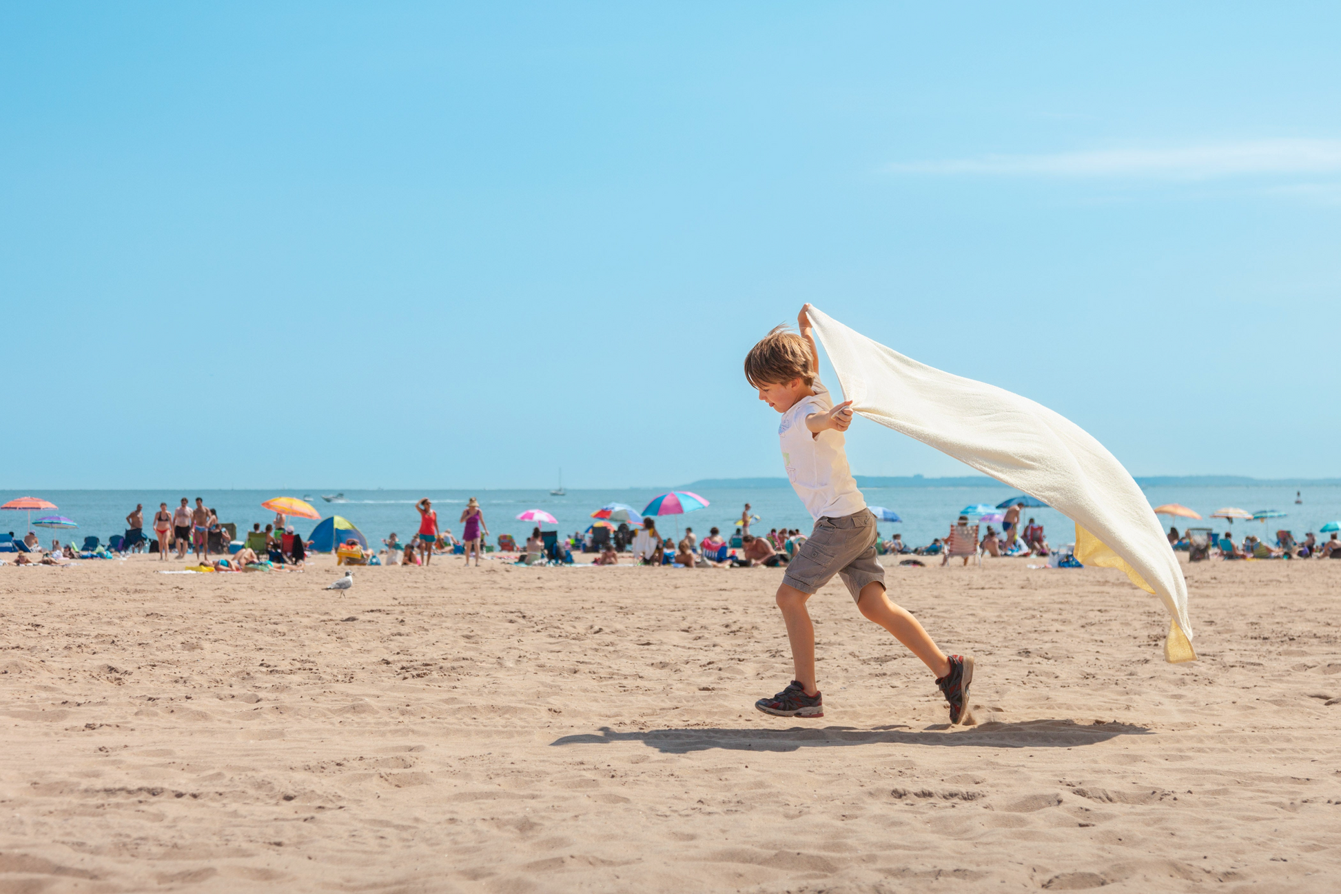 joyful color photo of little boy running with towel on the beach pretending to be super man on a hot summer day