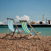 Load image into Gallery viewer, fine art color photo of striped sling back beach chairs on a pebble beach with brighton pier in distance

