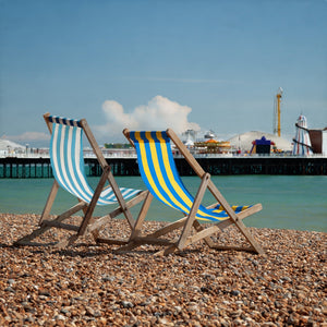 fine art color photo of striped sling back beach chairs on a pebble beach with brighton pier in distance