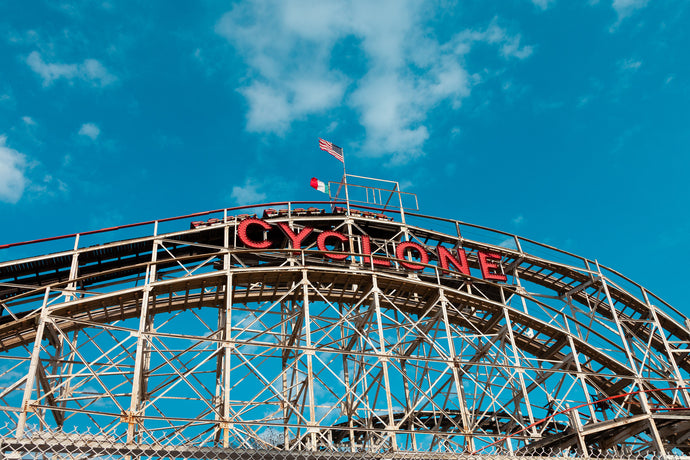 cyclone rollercoaster at the crest of the hill with blue sky, puffy clouds and italian and american flags in the wind