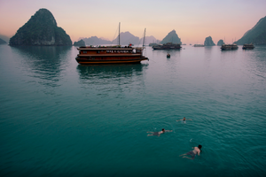 men take an early evening swim in halong bay vietnam surrounded by traditional boats and small islands