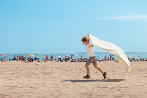 joyful color photo of little boy running with towel on the beach pretending to be super man on a hot summer day 