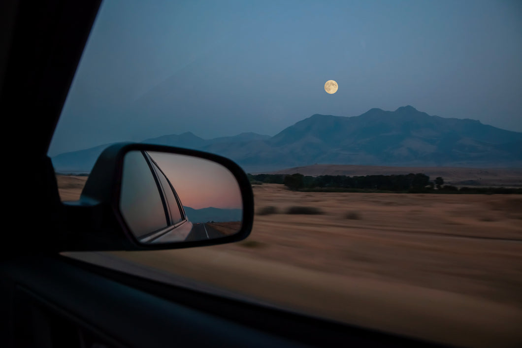 fine art landscape of full moon through a speeding car window in the rocky mountains