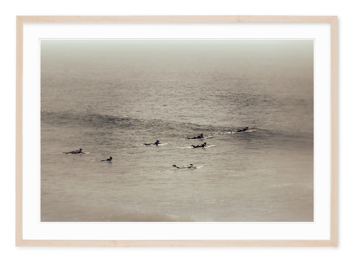 neutral tone fine art landscape of group of surfers heading out to catch waves