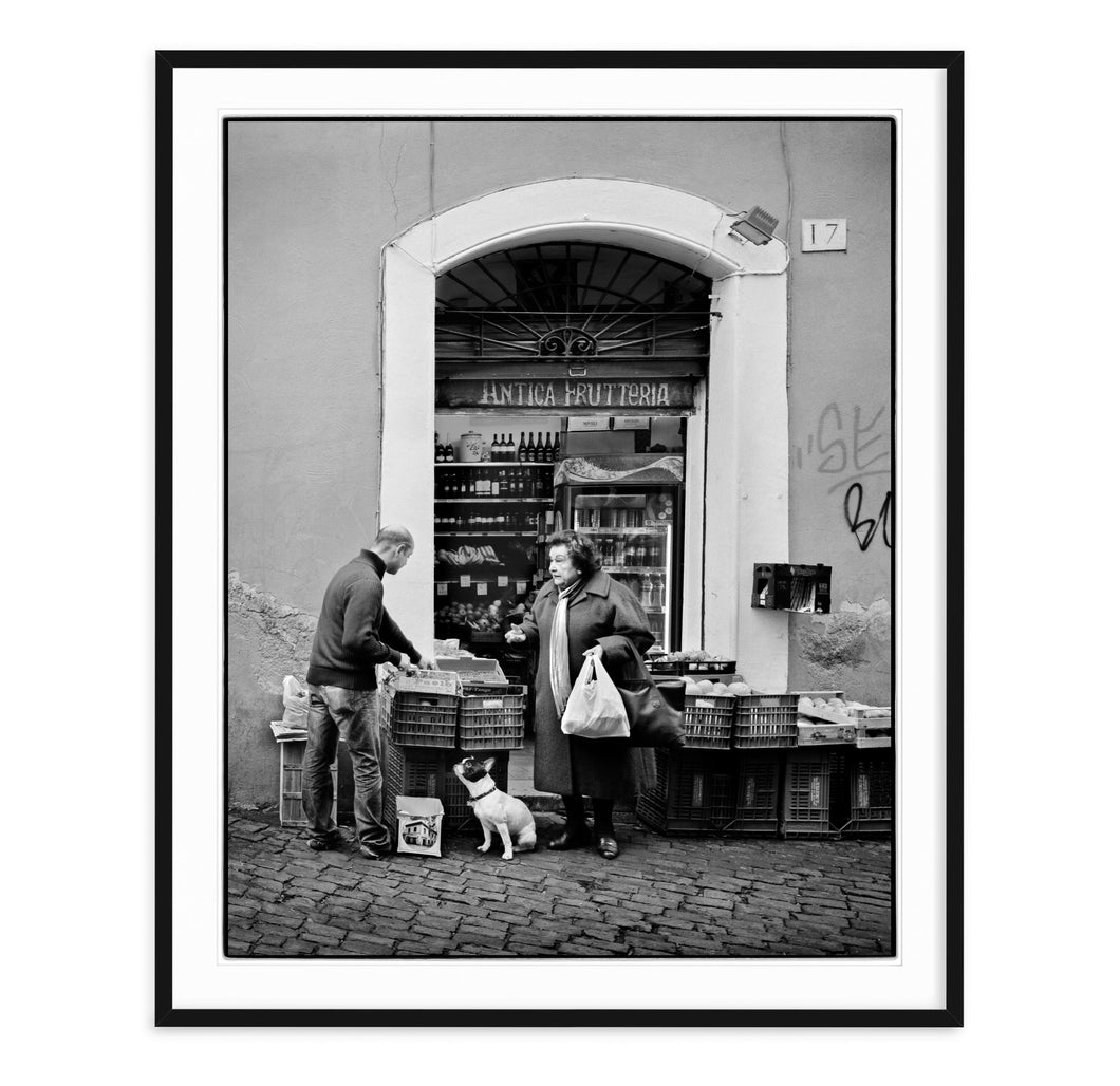 black and white fine art image in style of elliott erwitt with complaining woman and dog shopping at a traditional grocery in rome italy